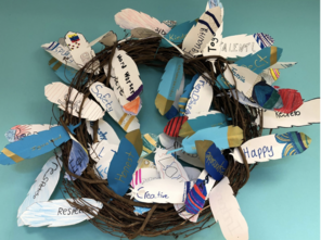 Image of a wreath with paper feathers on it. The paper feathers have writing on them that represent the values that each student's family cherishes.