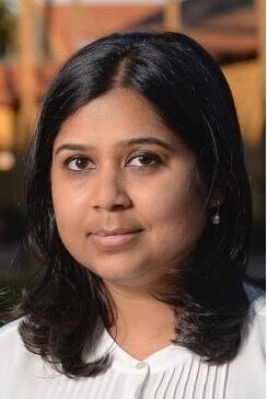 Vedika Khemani with layered shoulder-length dark hair framing her face, wearing a white blouse, and smiling slightly without showing teeth