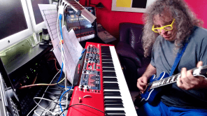 Mark Applebaum plays guitar while sitting at keyboard