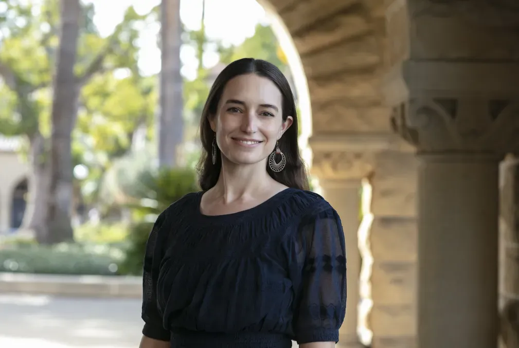 Lauren O'Connell wearing a black blouse and standing under an archway in one of the arcades on Stanford's Main Quad