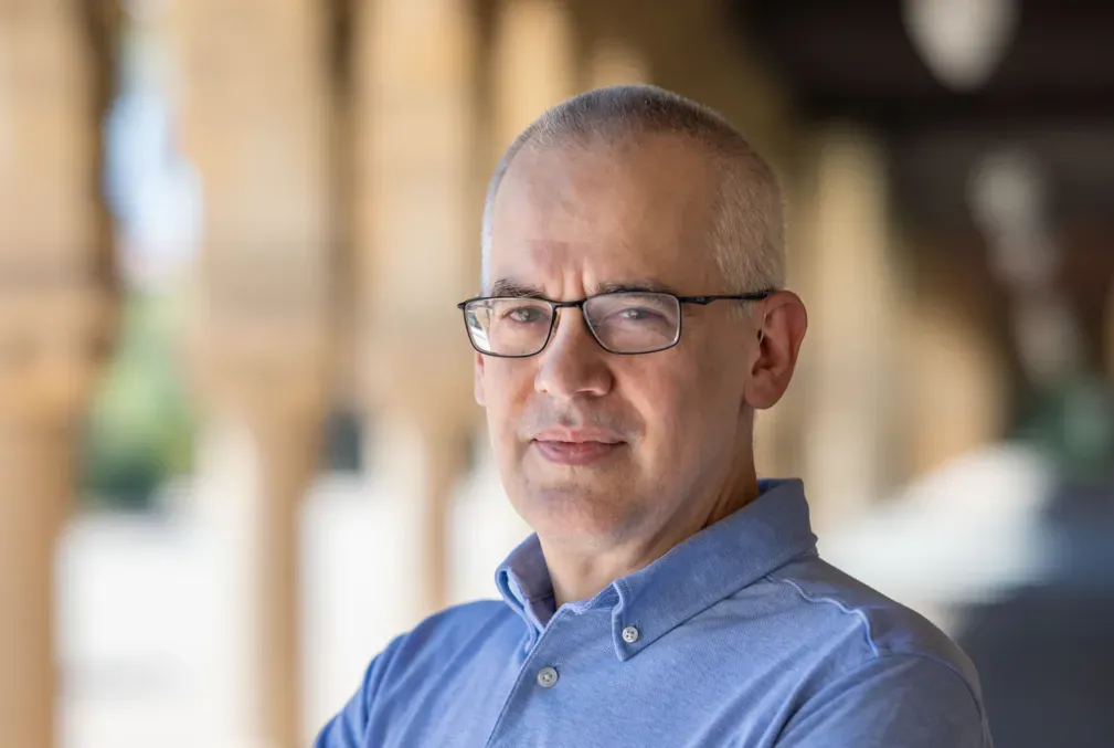 Matthew Sommer wearing a light-blue collared shirt standing under one of arcades on Stanford's Main Quad