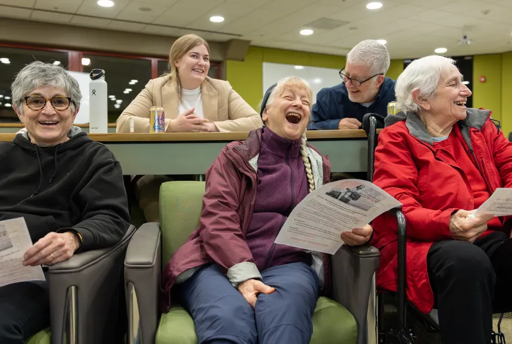 A group of five people sing and laugh together